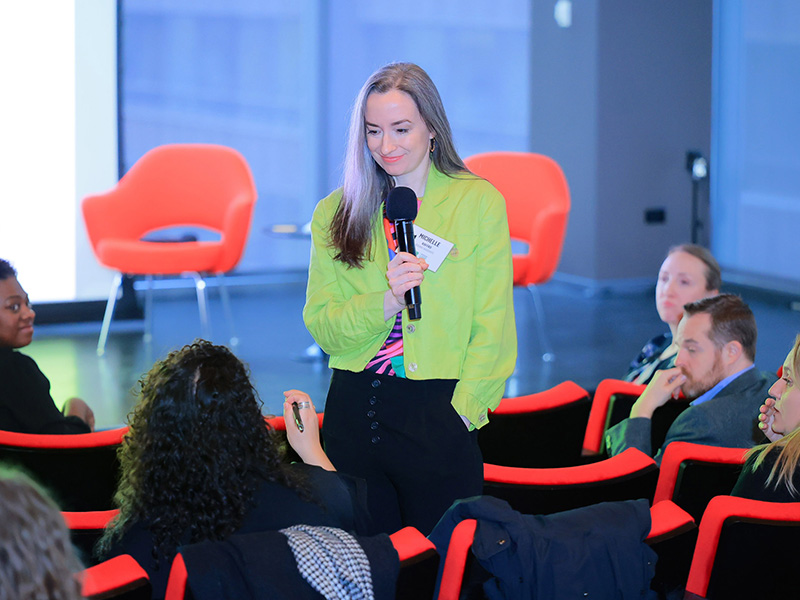 Woman holding a microphone speaking to audience Chicago Loop Alliance Marketing Lab; photo by Purple Photo